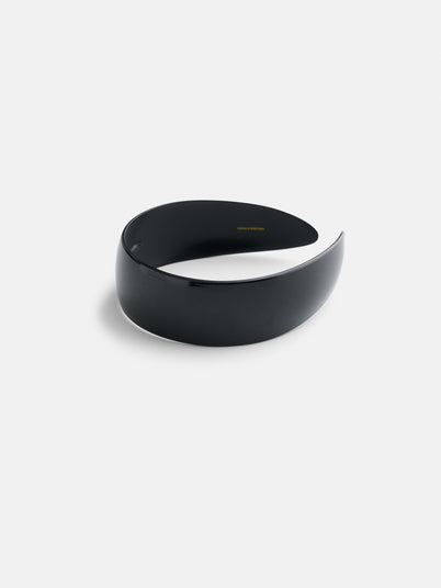 The Wide Headband, handcrafted from premium acetate, features a sleek, glossy black crescent shape and minimalist design with a slightly curved, wide structure. It is displayed on a plain white background.
