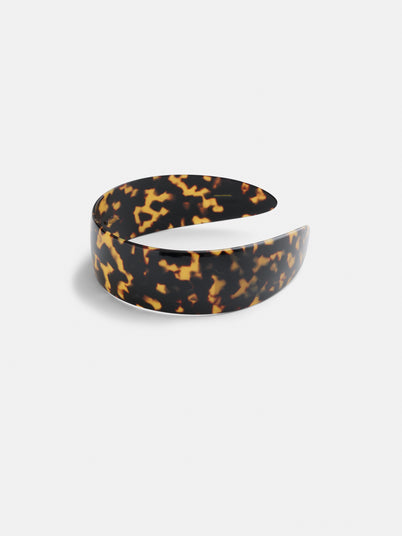A wide headband with a glossy tortoiseshell pattern in brown and amber tones, handcrafted in France and displayed on a plain white background.
