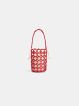 The Riviera Beaded Mini Bag is a small cylindrical purse with a cream base, encased in red knotted netting and finished with a matching red handle.