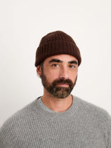 A bearded man wearing the Cashmere Beanie in warm brown and a gray sweater stands against a plain white background, looking directly at the camera with a neutral expression.