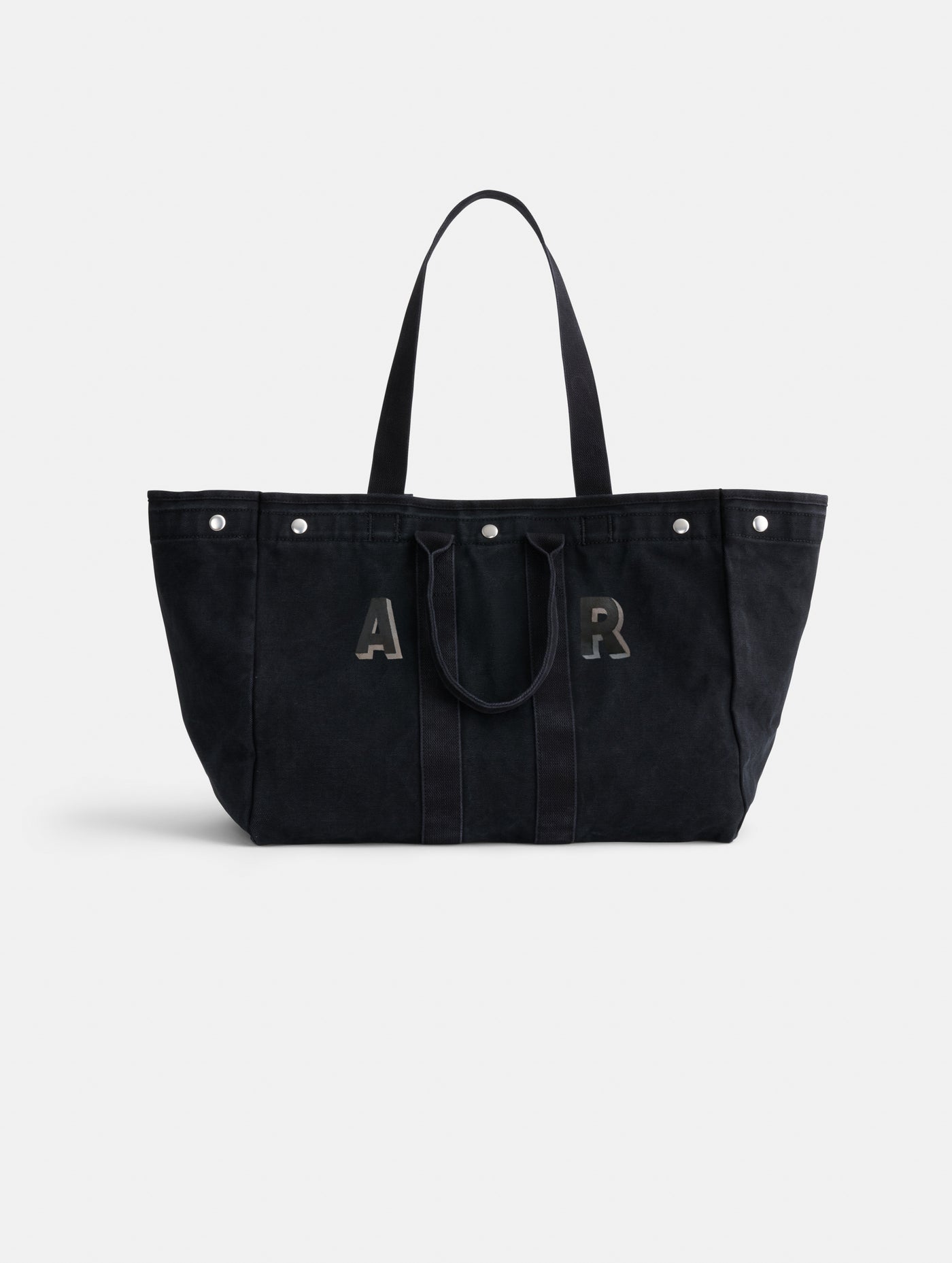 The Painted Perfect Weekend Tote is a spacious black canvas bag with two handles, silver grommets on top, and bold A and R letters displayed on the front.