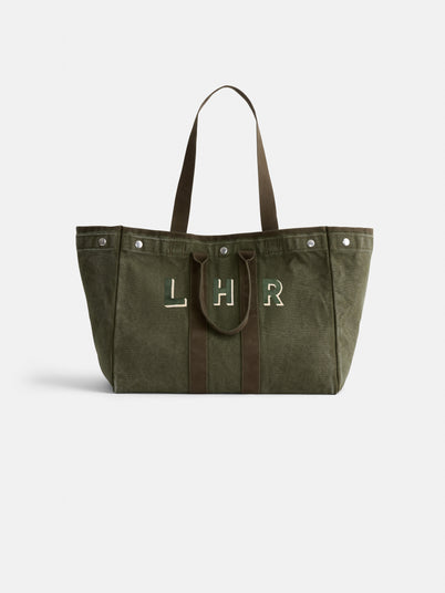 The Perfect Weekend Tote is a large olive green cotton bag with brown handles and trim, featuring "LHR" in white and green on the front. It includes personalized details and metal snaps near the top edges.