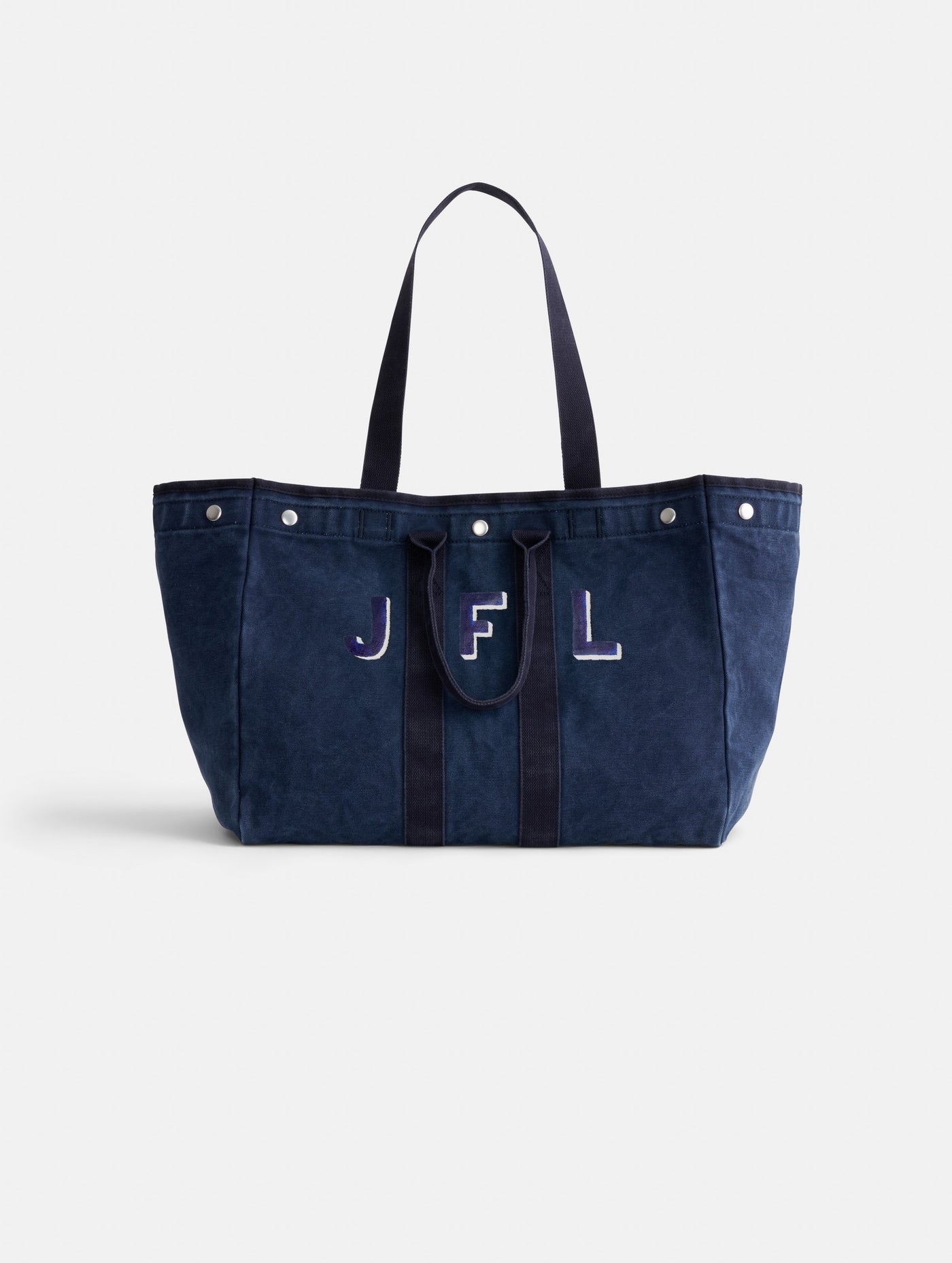 The Painted Perfect Weekend Tote is a spacious navy blue canvas bag with two handles, button accents on the top edge, and 