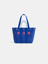 The Painted Perfect Weekday Tote is a blue bag with handles, featuring "MOM" in red and white letters on the front, shown against a plain white background.