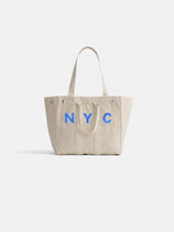 The Perfect Weekday Tote is a beige cotton bag with two handles and bold blue NYC lettering on the front, shown against a white background. Ideal for anyone looking for a stylish and customizable everyday tote.