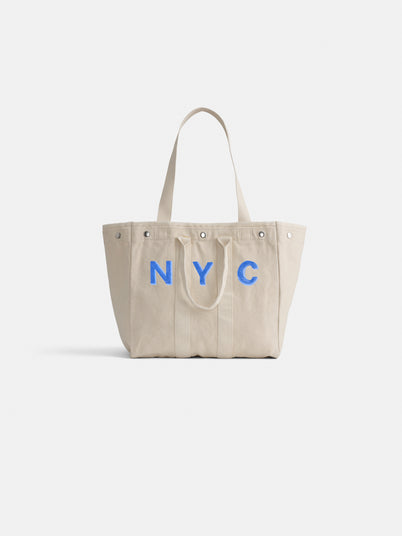The Perfect Weekday Tote is a beige cotton bag with two handles and bold blue NYC lettering on the front, shown against a white background. Ideal for anyone looking for a stylish and customizable everyday tote.