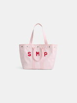 The Painted Perfect Weekday Tote is a light pink canvas bag with two handles and bold red "SMP" letters stitched on the front, displayed against a plain white background.