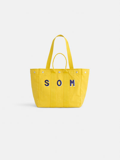 The Perfect Weekday Tote is a bright yellow cotton bag with two handles and bold blue "SOM" letters on the front, ideal for personalized style. Displayed against a plain white background.