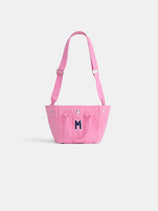 The Mini is a small pink cotton canvas tote with a front pocket, two handles, adjustable shoulder strap, and a dark blue "M" on the front—perfect for supporting breast cancer research. Shown on a plain white background.