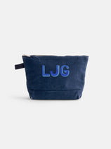 The Perfect Canvas Pouch—a navy blue pouch with a black side loop, embroidered LJG initials in blue and purple on the front—offers a stylish makeup bag inspired by subtle vintage military style, shown against a plain white background.