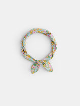 The Alex Mill x Liberty Bandana, a light blue floral scarf made from 100% cotton with pink, yellow, and green patterns, is tied in a loose knot on a white background—perfect for summer.