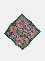 The Paisley Scarf In Silk features a vintage-inspired square design with intricate paisley and floral patterns in red, pink, yellow, and blue on a dark green background, shown flat on a white surface.