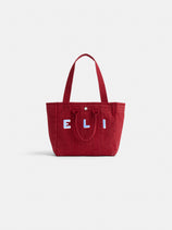 The Painted Perfect Daily Tote is a red bag with two handles, a front pocket, and "ELI" in white applique on the front. The background is plain white.