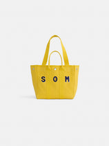 The Perfect Daily Tote is a bright yellow cotton bag with two handles and bold dark blue SOM letters on the front, shown against a white background. Both stylish and practical, it's ideal for everyday use.
