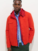 A man stands against a plain white background, wearing the Garment Dyed Work Jacket In Recycled Denim over a blue and white striped shirt. His expression is neutral, with his left hand in his jacket pocket.