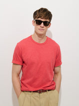 A man in sunglasses and beige pants models the Standard T-Shirt In Slub Cotton, a breathable red men's tee, standing against a plain white background with hands in his pockets and a slight smile at the camera.
