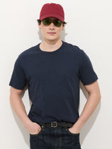 A person wearing a red cap, green sunglasses, the Standard T-Shirt In Slub Cotton (navy blue), and dark jeans stands against a plain white background with hands in their pockets.