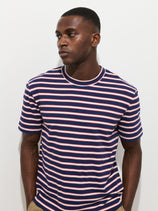 A man stands against a white background wearing the Crosby Striped Tee in navy blue, pink, and white heavy slub cotton and khaki pants. He looks slightly left with a neutral expression and his hands in his pockets.
