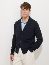A man with short brown hair wears the Alain Blazer In Cotton Linen over a light blue polo shirt and white pants, standing against a plain white background with a neutral expression.