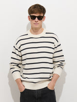 A person wears the Gabriel Pullover In Cotton Linen and black pants, standing against a plain white background with hands in their pockets and dark sunglasses.