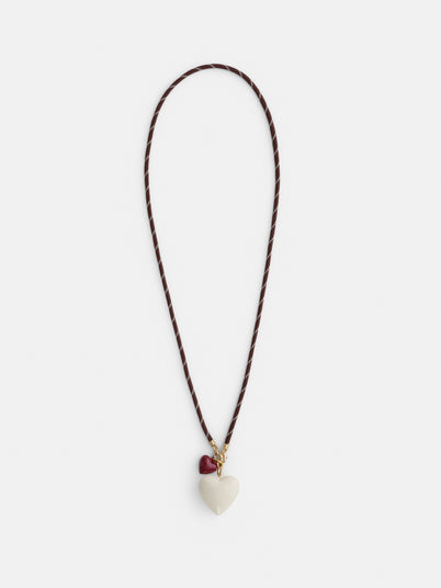 The Roxanne Assoulin Long Happy Cord Charm Necklace features a puffy white heart-shaped pendant, a smaller red heart charm near the clasp, and colorful dark brown cording.
