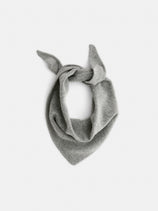 The Handkerchief Scarf In Wool is shown in light gray, folded into a triangle and tied with a loose knot, displayed against a plain white background.