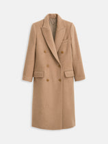 The Jamie Coat In Italian Wool is a long, double-breasted camel coat made in NYC, featuring notch lapels, brown buttons, front flap pockets, and a chest pocket. It’s showcased against a plain white background.