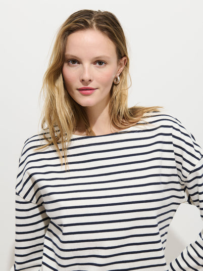 A woman with light brown hair wears the Avignon Striped Tee in Cotton and pearl earrings, standing against a plain white background and looking at the camera with a slight smile.