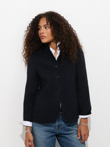 Wearing the Lafayette Jacket in Double-Faced Wool over a white shirt and jeans, a person with curly hair stands against a plain white background, looking to the side.