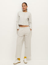 A woman stands against a white background wearing a light gray cotton double jersey long-sleeve buttoned top and matching Coco Sport Pant, paired with yellow socks, white sneakers, and her hands in her pockets for an effortless designer look.