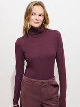 A woman models the Tissue Turtleneck In Cotton in purple, paired with high-waisted matching pants. She stands against a plain white background, gazing slightly to her left with a relaxed expression.