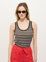 A woman with long light brown hair stands against a white background, wearing the Garcon Striped Tank In Linen Cotton, red high-waisted pants, and sunglasses. She faces forward.