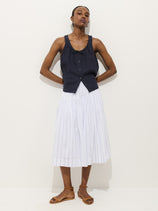 A person with short hair and minimal accessories stands against a white background wearing a sleeveless black button-up top, brown flat sandals, and the Hannah Striped Skirt in Cotton Voile.