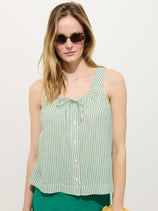 A woman in sunglasses wears the Sidney Stripe Top In Seersucker, a sleeveless, green-and-white striped button-down with a bow neckline and relaxed fit, standing against a plain white background.