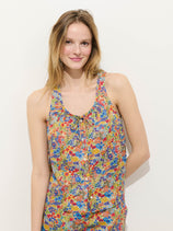 A person with long, light brown hair is smiling and wearing the sleeveless Sidney Floral Top in Liberty Fabric, featuring a colorful cotton floral print, while standing against a plain white background.