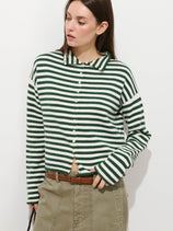A woman wearing the Taylor Striped Cardigan in Cotton Cashmere, a luxury green and white striped long-sleeve top with buttons, paired with an olive-green skirt, poses against a plain white background.