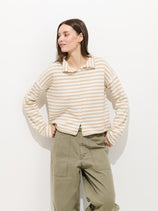 A woman stands against a white background wearing the Taylor Striped Cardigan in Cotton Cashmere with olive green high-waisted pants, her hands in her pockets as she looks to the side with a slight smile.