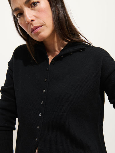 Woman with straight brown hair wears the Taylor Cardigan In Cotton Cashmere, black and oversized, looking slightly downward with a neutral expression against a plain light background.