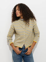 A person wearing the Taylor Striped Cardigan in Cotton Cashmere—featuring gray and yellow stripes—paired with blue jeans stands against a white background, looking to the side with one hand in their pocket.