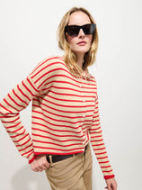 A woman in black sunglasses wears the Taylor Striped Cardigan in Cotton Cashmere—an oversized red-and-white striped sweater—paired with beige pants, standing against a plain white background.