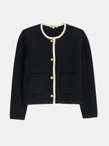 The Paris Sweater Jacket is a black, long-sleeve Milano stitch cardigan featuring a round neckline, cream trim, brass crest buttons, and two front pockets, shown on a white background.
