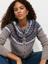 A woman with curly hair models the Charlotte Fairisle Sweater in Wool, featuring a blue, white, and brown vintage Fair Isle yoke. She sits against a white background, looking directly at the camera with a neutral expression.