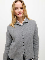 A woman with blonde hair wears the Taylor Cardigan in Cashmere over a white collared shirt, standing against a plain white background and smiling slightly at the camera.