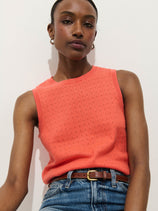 A woman wears the Odette Sweater Tank in Cotton Cashmere, styled with blue jeans and a brown belt, standing against a white background and looking confidently at the camera.