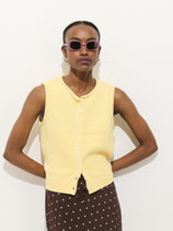 A person wearing the Taylor Vest In Cotton, a brown skirt with white polka dots, and pink sunglasses stands against a plain white background.