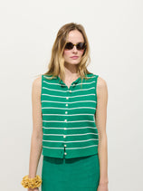 A woman with long hair and a yellow scrunchie on her left wrist wears the Taylor Striped Vest In Cotton, featuring green with white horizontal stripes, styled with sunglasses against a plain white background.