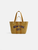 A Limited Edition Painted Perfect Weekday New York City Tote, featuring a tan canvas body, brown handles, and bold "NEW YORK CITY" lettering in navy blue on the front, displayed against a white background.